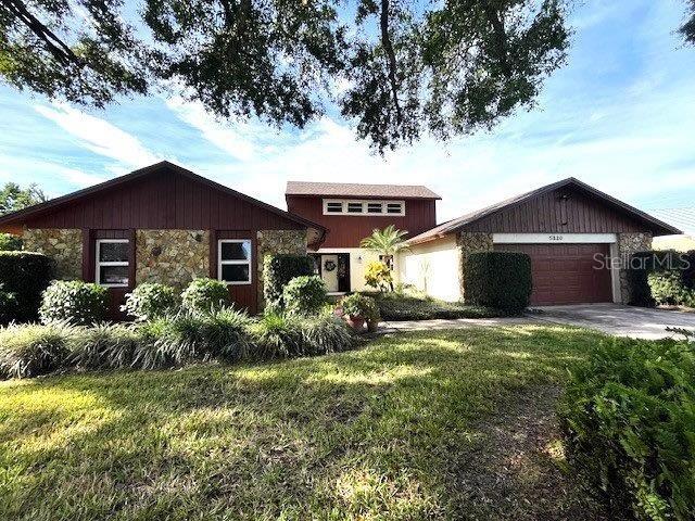 view of front of house with a garage, stone siding, concrete driveway, and a front yard