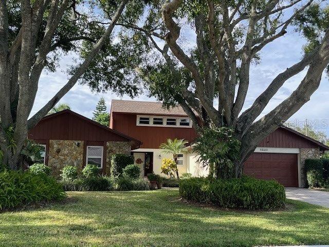 view of front of house with stone siding, driveway, a front lawn, and an attached garage