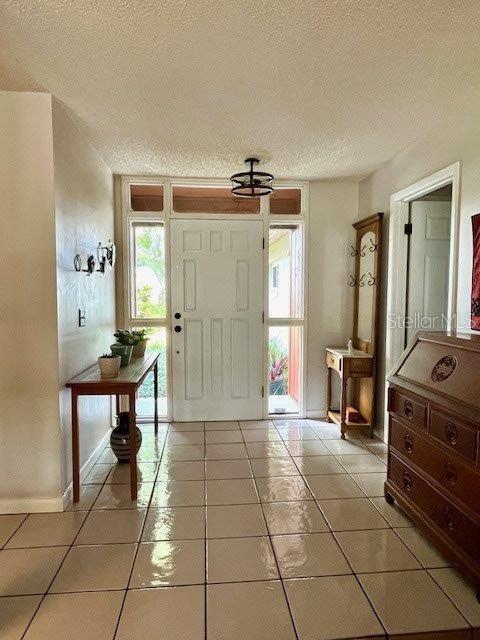 foyer with a textured ceiling, baseboards, and light tile patterned floors