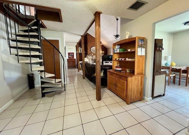 interior space featuring light tile patterned floors, visible vents, a textured ceiling, and stairs