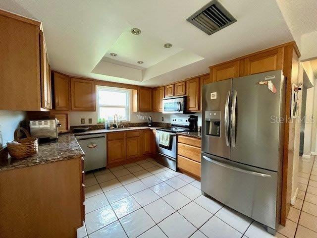 kitchen featuring visible vents, brown cabinetry, a raised ceiling, stainless steel appliances, and a sink