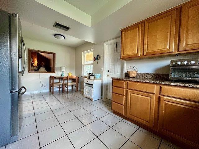 kitchen featuring brown cabinets, light tile patterned floors, visible vents, freestanding refrigerator, and dark stone counters