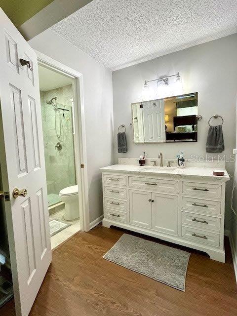 bathroom featuring a stall shower, toilet, wood finished floors, a textured ceiling, and vanity