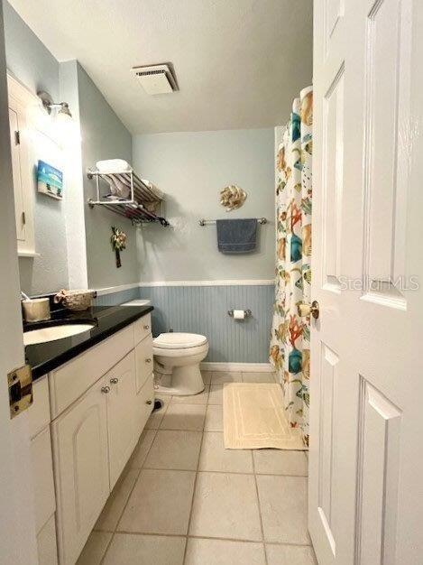 bathroom featuring tile patterned flooring, toilet, vanity, visible vents, and wainscoting