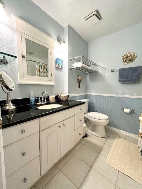 full bathroom featuring tile patterned flooring, toilet, a wainscoted wall, vanity, and visible vents