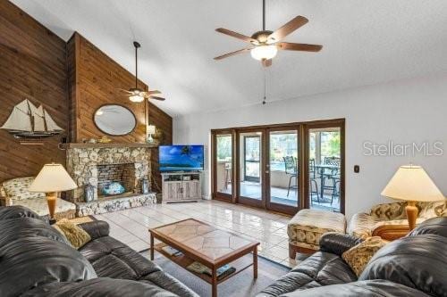 tiled living area featuring high vaulted ceiling, a stone fireplace, and wooden walls