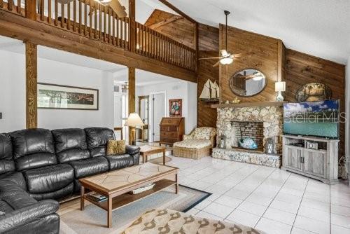 living room featuring ceiling fan, tile patterned flooring, wooden walls, a fireplace, and a towering ceiling