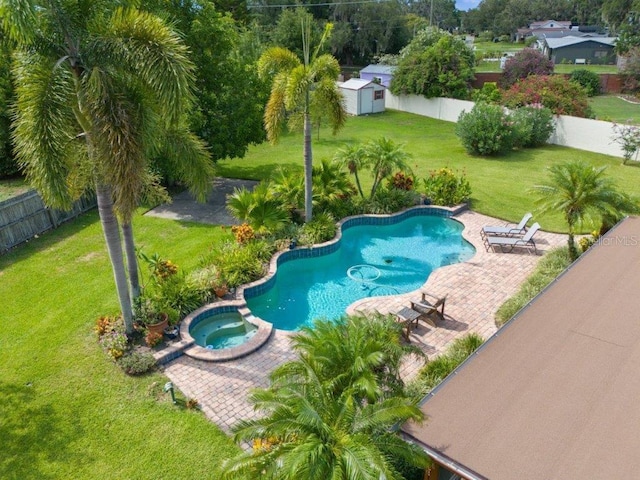 view of swimming pool with a patio, a fenced backyard, a pool with connected hot tub, a yard, and a storage unit