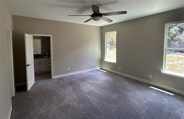 unfurnished bedroom featuring multiple windows, dark carpet, ensuite bath, and baseboards