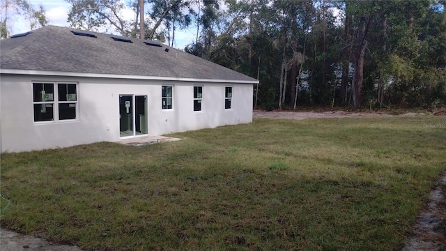 rear view of property with stucco siding, roof with shingles, and a yard