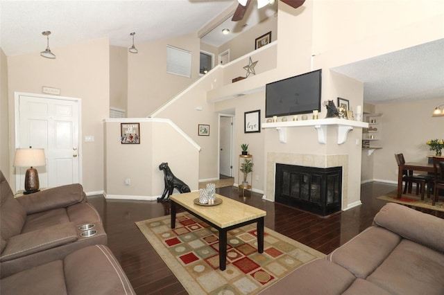 living room featuring stairway, wood finished floors, high vaulted ceiling, a tile fireplace, and baseboards