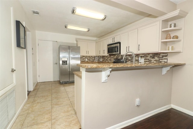 kitchen with a breakfast bar, open shelves, stainless steel appliances, visible vents, and a peninsula