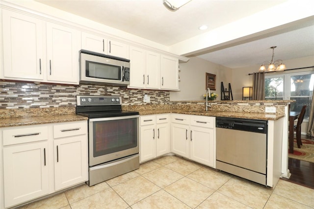 kitchen featuring light tile patterned flooring, stainless steel appliances, a peninsula, white cabinetry, and backsplash