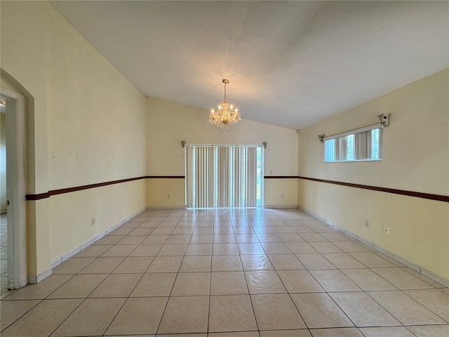 empty room with light tile patterned floors, lofted ceiling, a textured ceiling, a chandelier, and baseboards