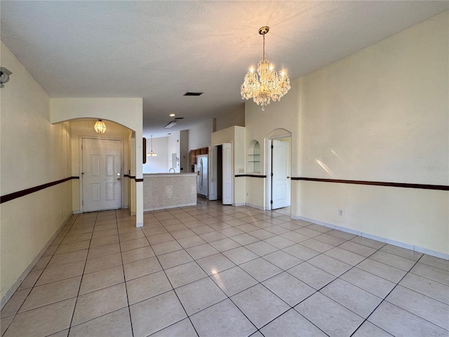 unfurnished room with light tile patterned floors, arched walkways, visible vents, and an inviting chandelier