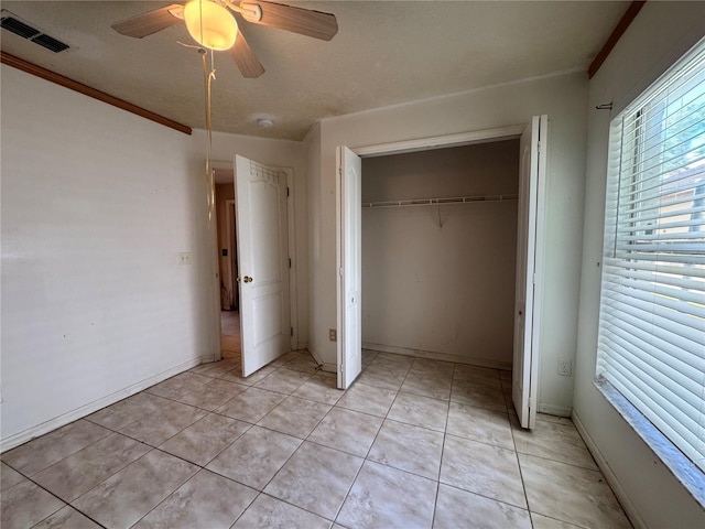 unfurnished bedroom featuring light tile patterned floors, visible vents, a ceiling fan, ornamental molding, and a closet