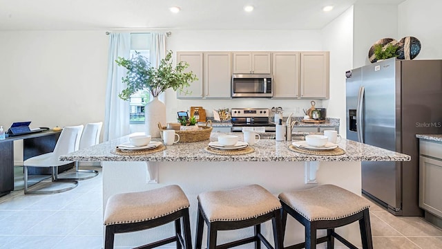 kitchen featuring light stone counters, a breakfast bar, light tile patterned floors, appliances with stainless steel finishes, and a kitchen island with sink