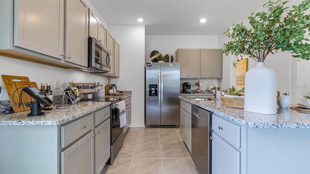 kitchen featuring light tile patterned floors, light stone counters, gray cabinetry, a sink, and appliances with stainless steel finishes