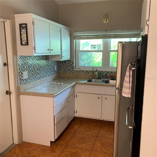 kitchen featuring light countertops, decorative backsplash, freestanding refrigerator, white cabinets, and a sink