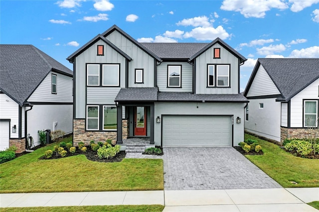 modern inspired farmhouse featuring an attached garage, stone siding, decorative driveway, a front lawn, and board and batten siding