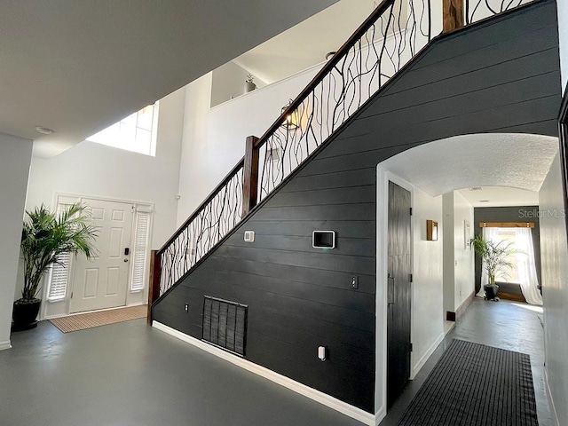 stairs with arched walkways, a high ceiling, baseboards, and finished concrete floors