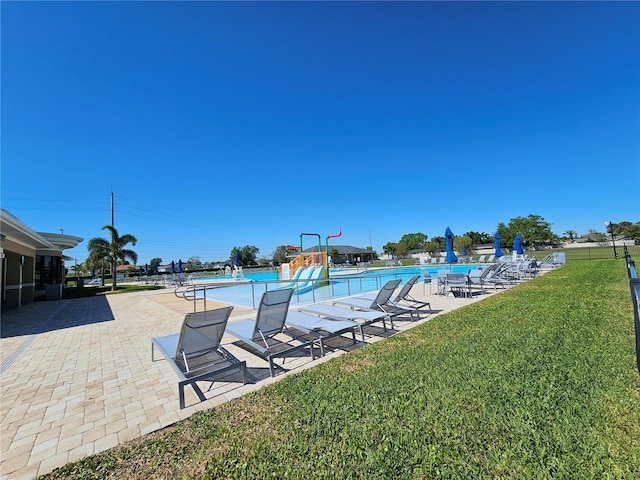 pool with a water play area, a patio, a lawn, and a water slide