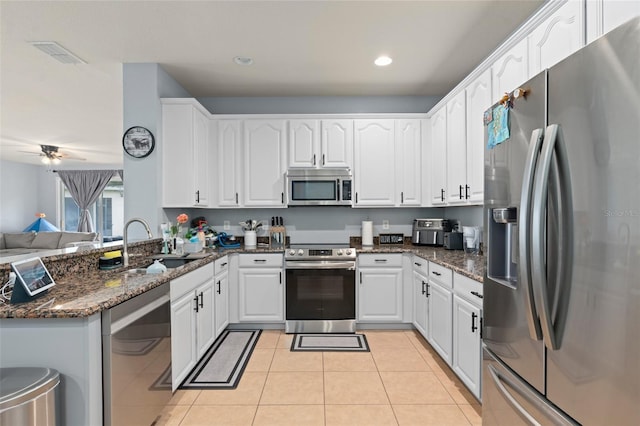 kitchen with stainless steel appliances, a sink, visible vents, white cabinetry, and dark stone countertops