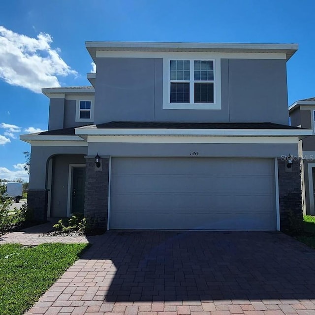 traditional-style house featuring a garage, stone siding, decorative driveway, and stucco siding