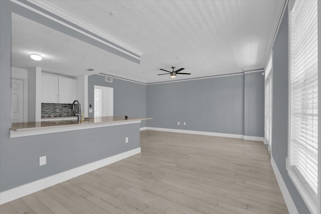 unfurnished living room featuring light wood-style flooring, ceiling fan, a textured ceiling, crown molding, and a sink