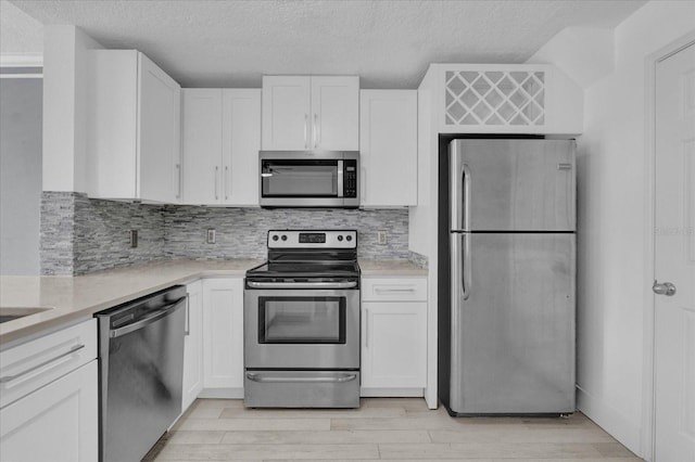 kitchen with light wood finished floors, tasteful backsplash, appliances with stainless steel finishes, white cabinetry, and a textured ceiling