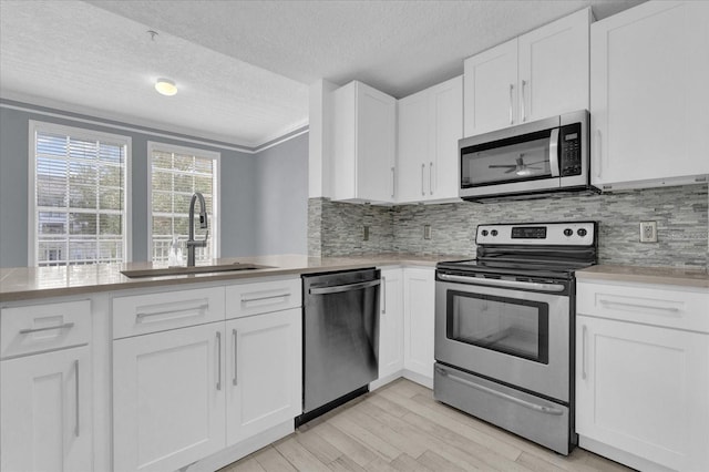 kitchen with white cabinets, light wood-style flooring, stainless steel appliances, light countertops, and a sink