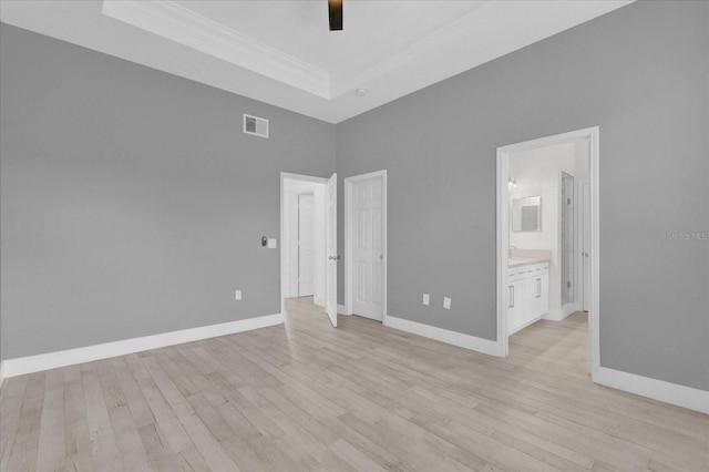 unfurnished bedroom featuring a tray ceiling, light wood-type flooring, visible vents, and baseboards