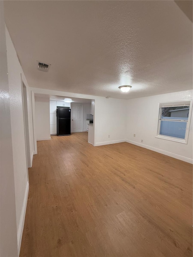 unfurnished living room with baseboards, visible vents, a textured ceiling, and light wood finished floors