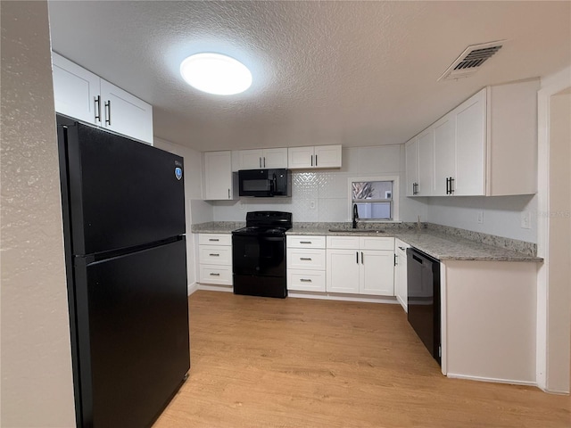 kitchen featuring visible vents, white cabinets, light wood-style flooring, black appliances, and a sink