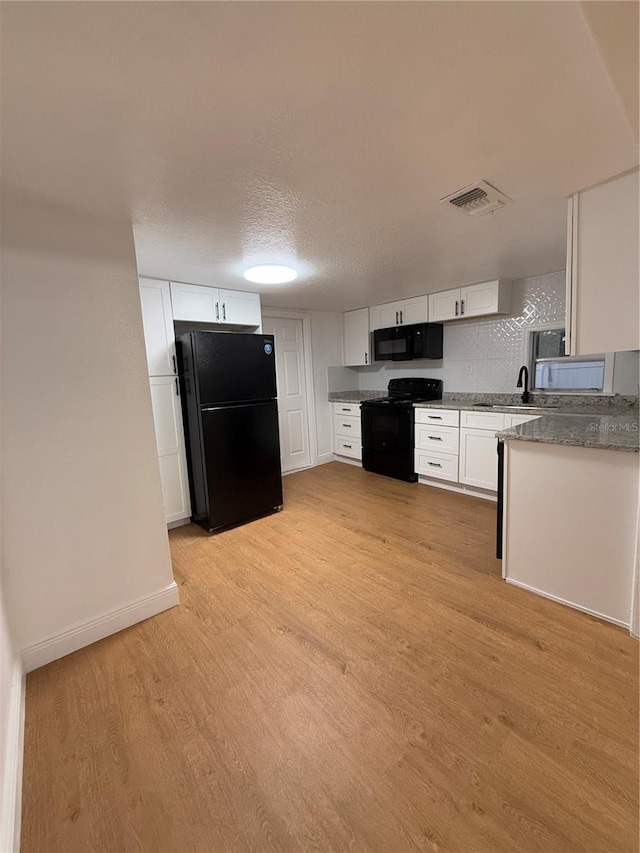 kitchen featuring visible vents, light wood-style floors, black appliances, white cabinetry, and a sink