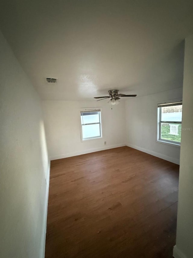 empty room with dark wood-style flooring, a healthy amount of sunlight, visible vents, and baseboards