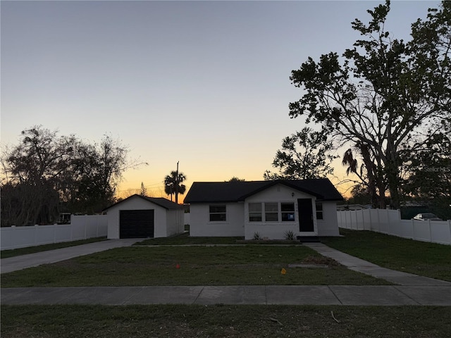 view of front facade with a yard, a detached garage, fence, an outdoor structure, and driveway