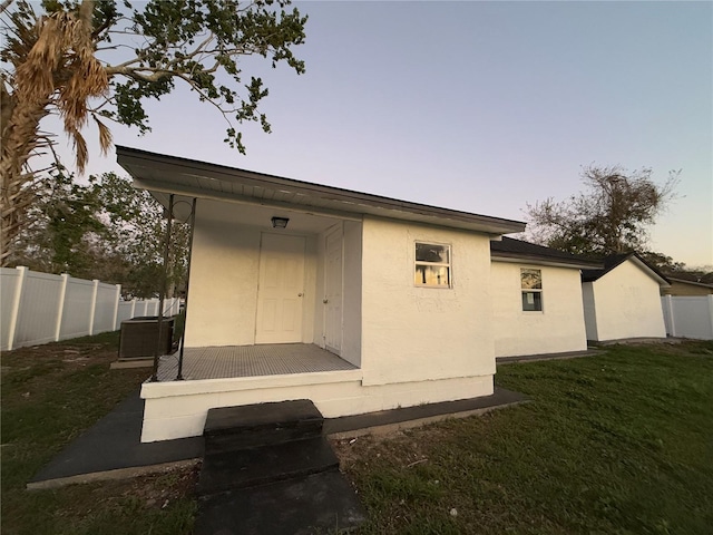 back of property with cooling unit, a lawn, fence, and stucco siding