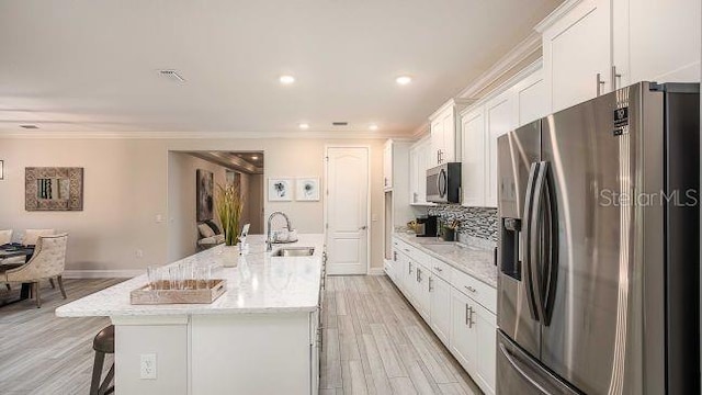 kitchen with light stone counters, stainless steel appliances, white cabinets, a sink, and an island with sink