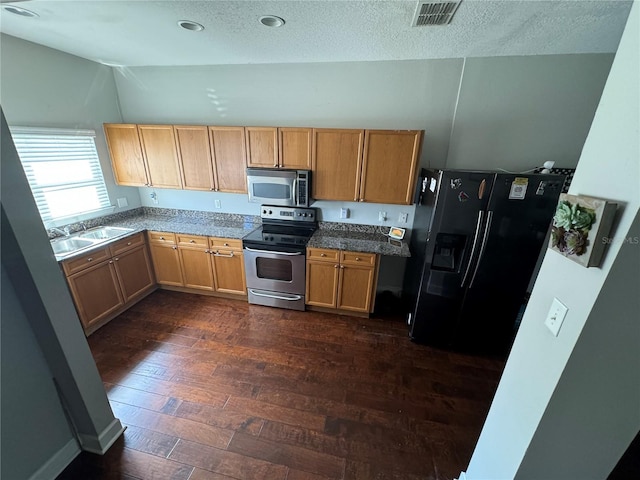 kitchen featuring a textured ceiling, stainless steel appliances, a sink, visible vents, and dark wood finished floors