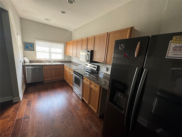 kitchen with a textured ceiling, dark wood-style flooring, a sink, baseboards, and appliances with stainless steel finishes