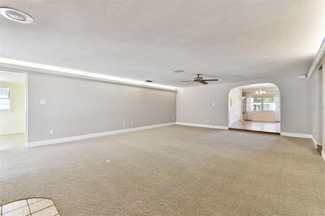 unfurnished living room featuring arched walkways, ceiling fan, light carpet, and a wealth of natural light