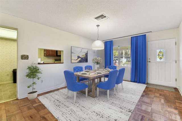 dining space with a textured ceiling, visible vents, and baseboards