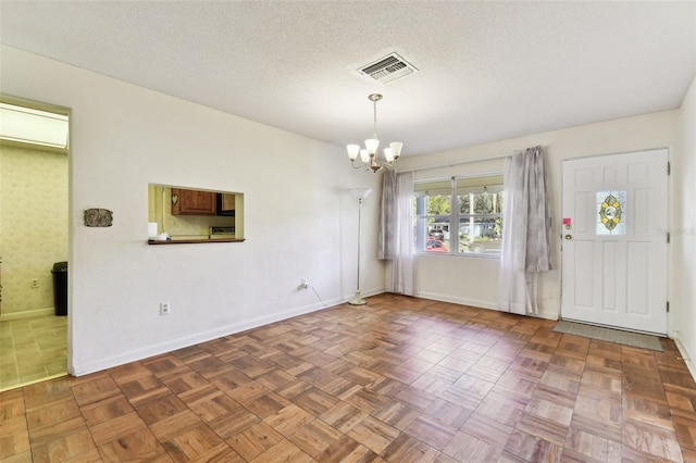 interior space with a textured ceiling, a chandelier, visible vents, and baseboards