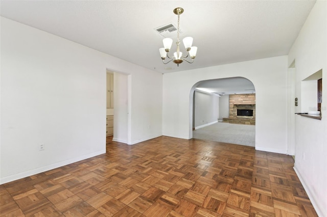 unfurnished room featuring baseboards, a fireplace, visible vents, and a notable chandelier