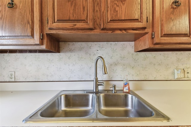 room details with wallpapered walls, light countertops, a sink, and brown cabinetry