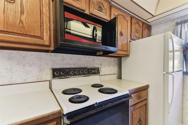 kitchen featuring brown cabinetry, electric range oven, and wallpapered walls