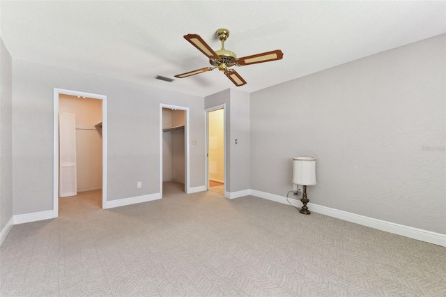 unfurnished bedroom featuring baseboards, a walk in closet, a ceiling fan, and light colored carpet