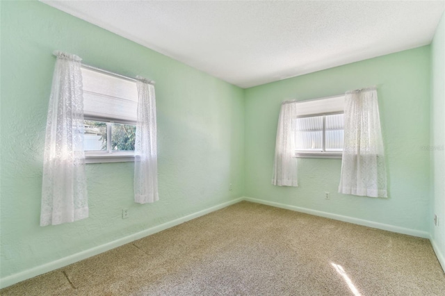 carpeted spare room featuring a textured ceiling and baseboards