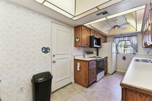 kitchen with white appliances, wallpapered walls, visible vents, ceiling fan, and a sink